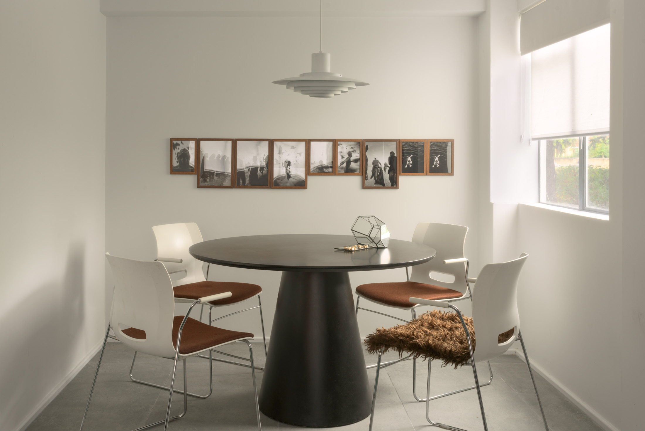 Sculptural dining table beneath a pendant light and framed photography